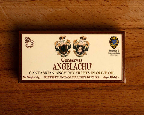 A tin of anchovies in a rectangular brown and cream box against a wood background