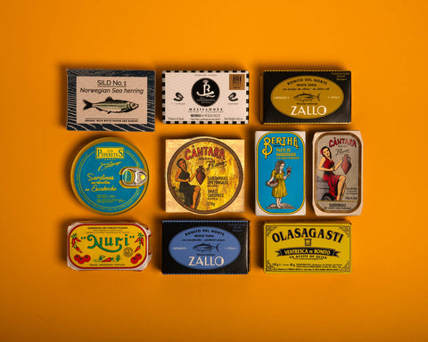 A selection of brightly-packaged tinned fish on a yellow backdrop