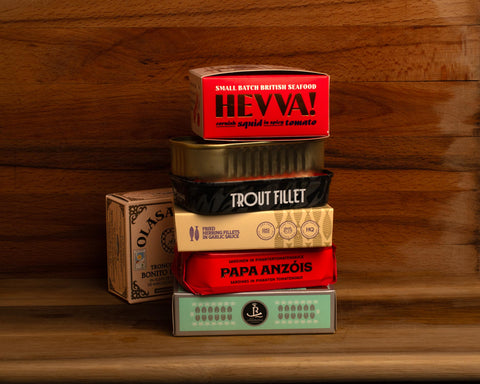 Seven brightly coloured tins of fish against a wood background