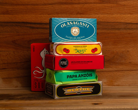 Six tins of brightly packaged tinned fish against a wood background