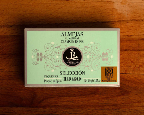 A tin of clams with green and silver card packaging against a wood background.