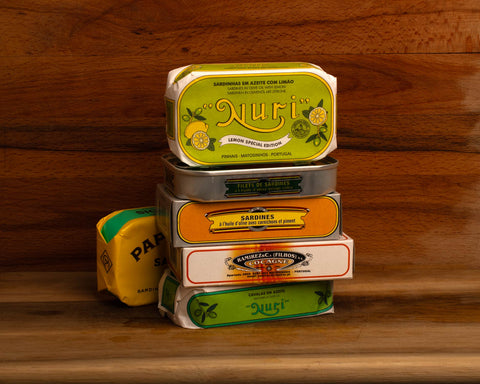 A selection of colourfully-packaged tinned sardines against a wooden background.