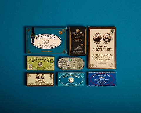 A gift box with different types of anchovies. all of them come from the Cantabrian sea in Spain. They are perfectly arranged on a blue background.