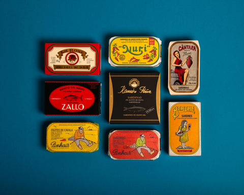 Spanish and Portuguese tinned fish in colourful and classic packaging arranged on a light blue backdrop.